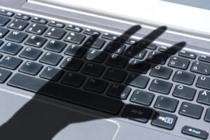 Dark shadow of a hand reaches for computer keyboard symbolizing cyber crime Dark shadow of a hand reaches for computer keyboard symbolizing cyber crime
