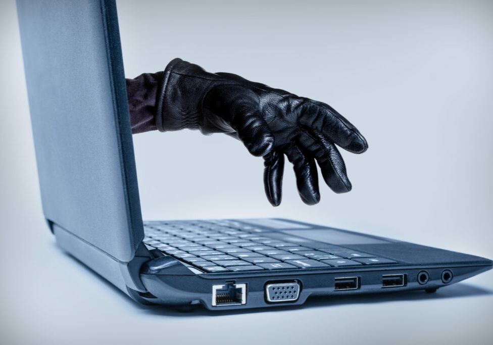 A gloved hand reaching out through a laptop, signifying a cybercrime or Internet theft while using Internet media.