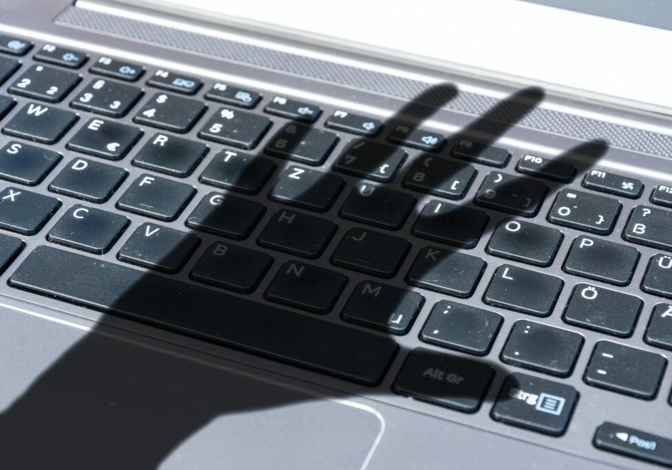 Dark shadow of a hand reaches for computer keyboard symbolizing cyber crime